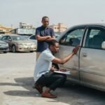 First-time Nigerian car buyer inspecting door panel gap on a tokunbo sedan at a car dealer's yard