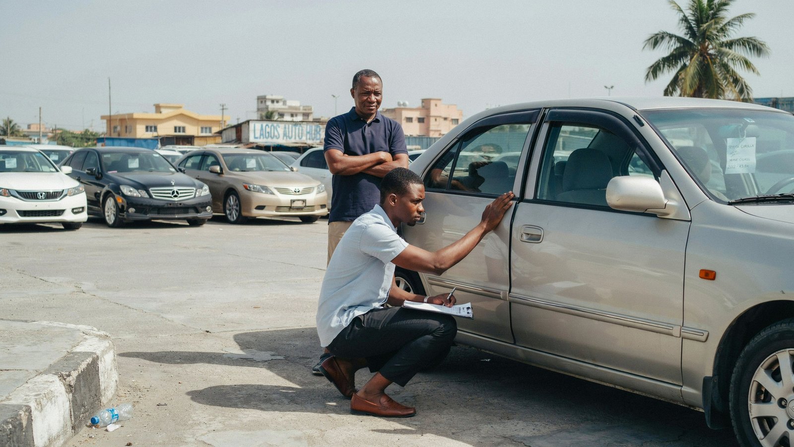 First-time Nigerian car buyer inspecting door panel gap on a tokunbo sedan at a car dealer's yard