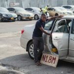 Nigerian car buyer closely inspecting the door seam of a used sedan for accident damage